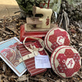 A pincushion kit displayed with fabrics and a sewing machine in the background, set against a natural outdoor setting.