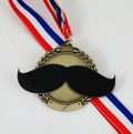 A novelty medal featuring a black mustache graphic over a gold laurel wreath design, suspended from a red, white, and blue ribbon on a plain white background.