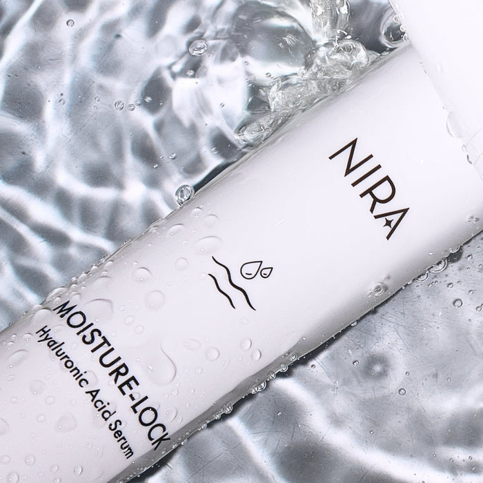 Close-up of NIRA Skincare Bundle hyaluronic acid serum bottle with water droplets on reflective surface