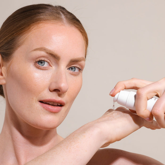 Woman applying serum from NIRA Skincare Bundle pump bottle to her hand, showcasing glowing skin and beauty routine.