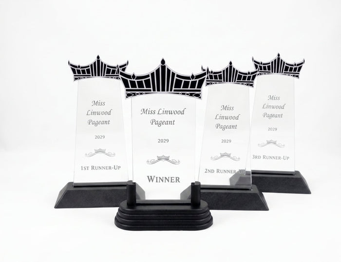 Four clear acrylic trophy plaques with black decorative finials and black bases, arranged in a row on a white studio background. (AI Generated)