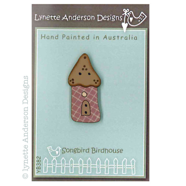 A hand painted wooden button with a brown roof, plaid pattern, and a door, on a blue background with 'Lynette Anderson Designs' and 'Songbird Birdhouse' text.