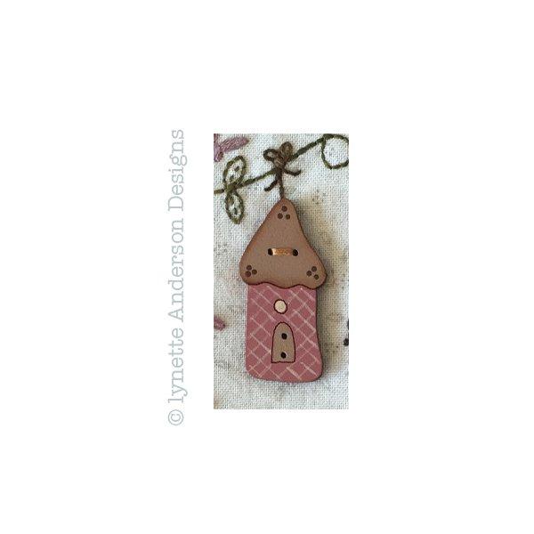 A hand painted wooden button with a brown roof, plaid pattern, and a door, on a blue background with 'Lynette Anderson Designs' and 'Songbird Birdhouse' text.